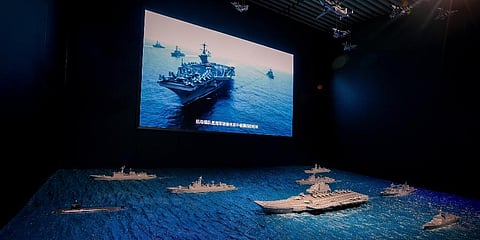 A TV screen showing the USÂ Navy fleet sail in formation near the models of Liaoning aircraft carrier with navy frigates and submarines on display at the military museum in Beijing. (Photo | AP)
