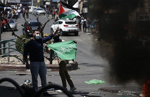 Palestinians demonstrators wave their national flag (Top) and green Hamas banner (bottom) during protests against Israel's occupation, in the occupied West Bank town of Hebron May 18. (Photo | AFP)