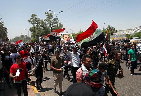 Anti-government protesters chant slogans as they hold posters of slain activist Ehab Wazni outside the Green Zone (Photo | AP)