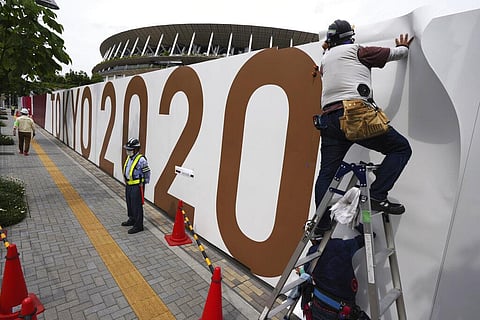 Workers paste the overlay on the wall of the National Stadium, where opening ceremony and many other events are scheduled for the postponed Tokyo 2020 Olympics. (Photo | AP)