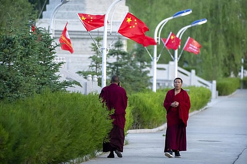Monks walk along a sidewalk path lined with Chinese flags at the Tibetan Buddhist College near Lhasa in western China's Tibet Autonomous Region, Monday, May 31, 2021.
