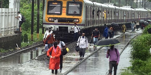 People walk on the waterlogged railway tracks after local trains services were affected due to heavy rain, at Sion in Mumbai. (Photo | PTI)