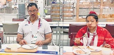Weightlifting coach Vijay Sharma and Mirabai Chanu at the Games Village in Tokyo on Friday. The duo is divided by a glass barrier as a precautionary measure against Covid