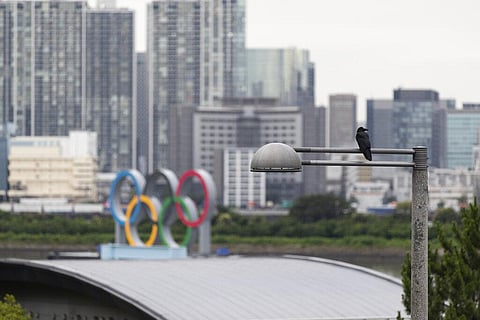 A crow perches on a light pole near the statue of the Olympics rings in Tokyo on Thursday, July 1, 2021. (Photo | AP)