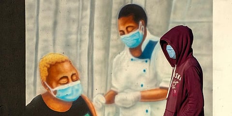 A man wearing a face mask to prevent the spread of coronavirus, walks past a mural promoting COVID-19 vaccinations in South Africa. (Photo | AP)