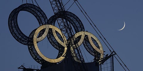 A worker labours to assemble the Olympic Rings onto of a tower on the outskirts of Beijing, China.(Photo | AP)