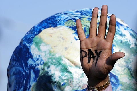 In this representational image, a hand reads 'pay' calling for reparations for loss and damage at the COP27 U.N. Climate Summit in Egypt, Nov. 18, 2022. (Photo | AP)