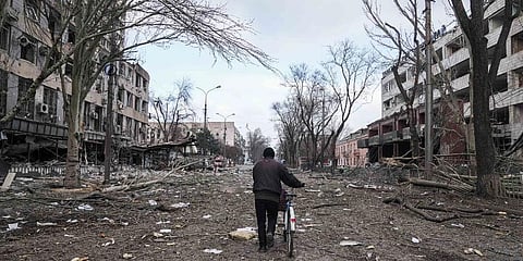 A man walks with a bicycle in a street damaged by shelling in Mariupol, Ukraine. (Photo | AP)