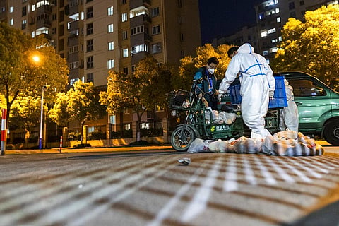 Deliverymen wearing protective suits carry bags of food at the gate of a residential community in Shanghai. (File Photo | AP)