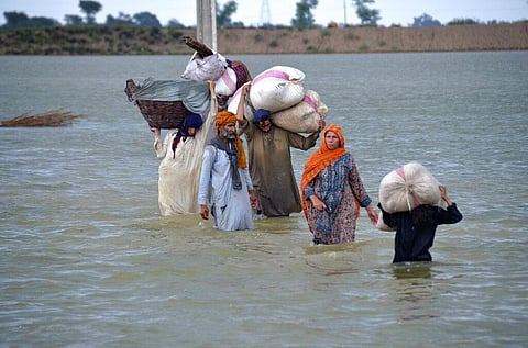 A displaced family wades through a flooded area after heavy rainfall, in Jaffarabad