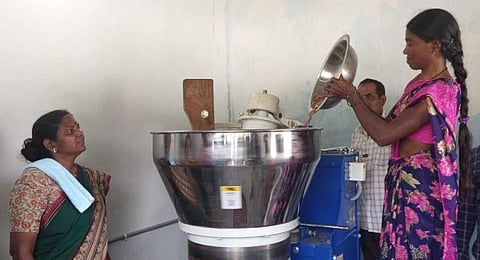 Women are seen pouring Mahua seeds into a grinder.