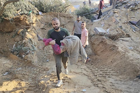 A Palestinian carries a child killed in Israeli airstrikes in Deir el-Balah Gaza Strip, Sunday, Oct 15, 2023. (Photo | AP)