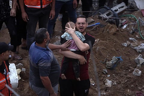 FILE: A Palestinian man cries while holding a dead child who was found under the rubble of a destroyed building following Israeli airstrikes in Nusseirat refugee camp. (Photo | AP)