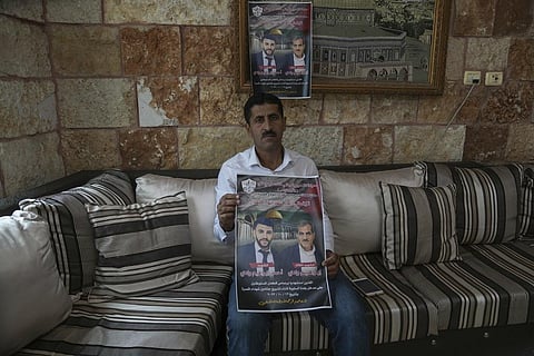 Abdelazim Wadi holds up a poster of his brother Ibrahim Wadi and his nephew, Ahmed Wadi, who were killed by Israeli settlers during a funeral procession on Oct 12 in the West Bank. (AP)