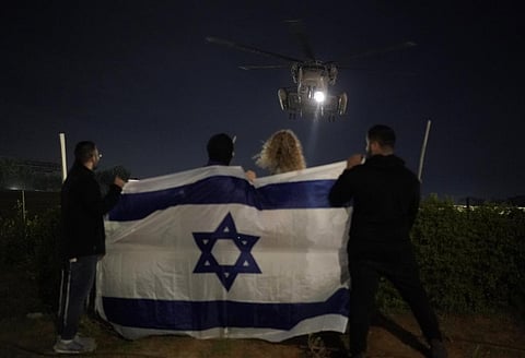 People holding an Israeli flag watch the arrival of a helicopter transporting Israeli hostages released by Hamas at the Sheba Medical Center in Ramat Gan, Israel, Tuesday Nov. 28, 2023. (Photo | AP)
