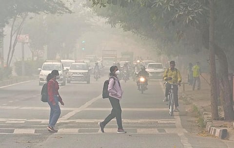 Students wearing masks cross a road amid hazy weather conditions in New Delhi. (Photo | PTI)