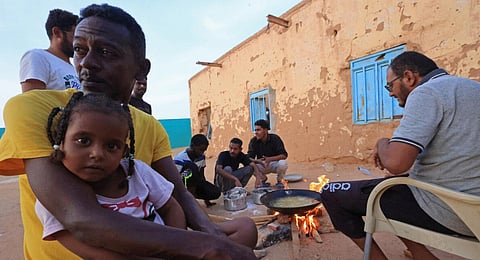 People sit around food cooking on a bonfire at a school that has been transformed into a shelter for people displaced by conflict in Sudan. (Photo | AFP)