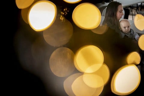 Vlada Yushchenko, a 19-year-old Ukrainian refugee, holds her son Daniel, seen through the lights of a Christmas tree, during an interview with AP in Brasov, Romania, Feb. 2, 2023. (Photo | AP)