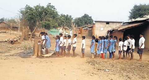 Students stand in a queue to collect drinking water from the village stand post at Rampara