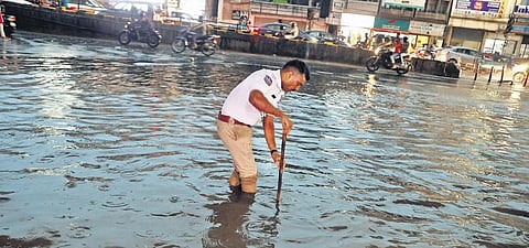 A traffic cop tries to clear a blocked manhole near the Prakash Nagar Metro Station following a heavy rain in Hyderabad on Monday evening /| Sri Loganathan Velmurugan