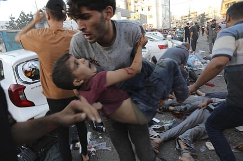 An injured Palestinian boy is carried from the ground following an Israeli airstrike outside the entrance of the al-Shifa hospital in Gaza City. (Photo | AP)