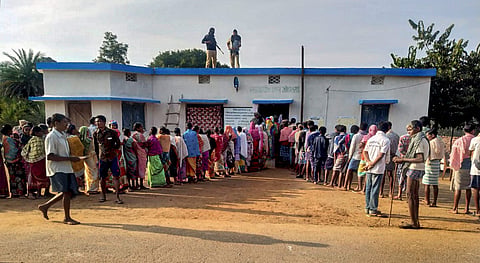Security personnel stand guard as voters wait in queues to cast their votes during the first phase of Assembly elections in Chhattisgarh. (Photo| PTI)