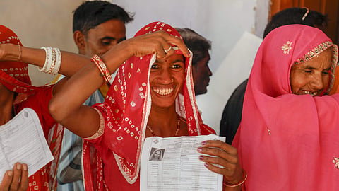 A voter smiles as she shows identity card during the elections at a polling station in Ajmer.
