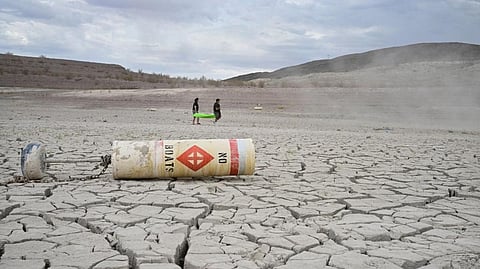 A buoy that reads ‘No Boats’ lays on cracked dry earth that was once part of Lake Mead in Nevada. In the background, people carry a boat to reach the reservoir’s receding shoreline on July 23. Photo: FREDERIC J BROWN/AFP via Getty Images