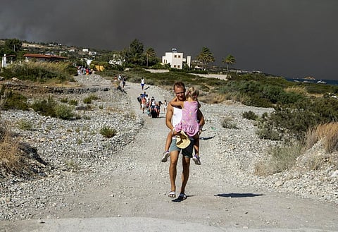 A tourist carries a child away from the wildfire on Rhodes. Photo: Lefteris Damianidis / AP