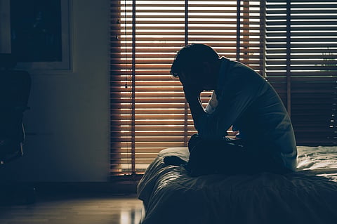 Man sitting with his head in hands on the bed in the dark bedroom with a low light environment and a vintage tone