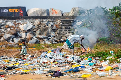 A girl plays in piles of trash while her mother burns it on the beach of Kollam, Kerala. IStock photo for representation