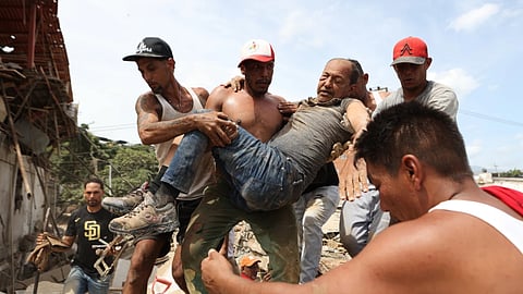 Neighbors carry a man rescued from the rubble of a collapsed building the day after earthquakes struck La Guaira, Venezuela
