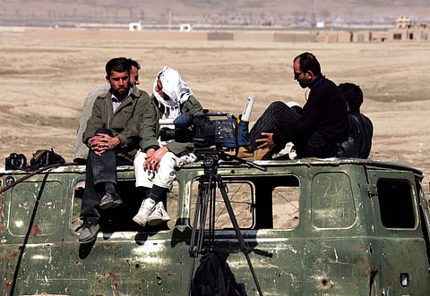 Five local journalists wait on the wreckage of a minibus while reporting on an uprising of Taliban prisoners in Pul-e-Charkhi prison, near Kabul, in 2006.