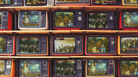 An illustration of TV screens stacked one on top of the other on wooden shelves. The screens are playing stills from Sri Lanka's former labour minister Mervyn Silva when he forcibly entered the state-owned Sri Lanka Rupavahini Corporation and assaulted the news director. Pictured is the angry crowd outside the offices, Mervyn Silva trying to pacify angry Rupavahini staffers and screengrabs of the news coverage.