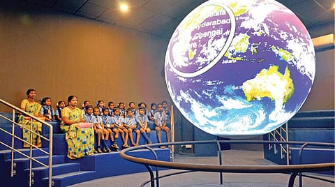 கோள வடிவ திரையில் பூமியைப் பற்றிய காட்சிகளை காணும் மாணவர்கள்.