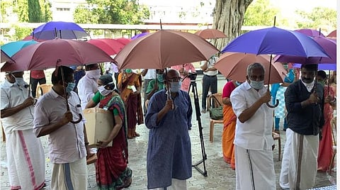 குடைபிடித்தபடி நிற்கும் கேரள அமைச்சர்கள் தாமஸ் ஜசக், மொய்தீன் மற்றும் கிராம மக்கள்.