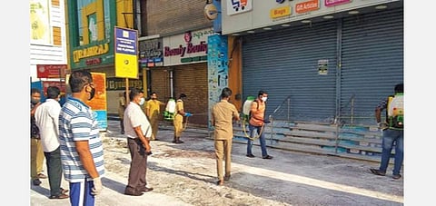 கோவை கிராஸ்கட் சாலை பகுதியில் மூடப்பட்டுள்ள கடைகளுக்கு முன் கிருமிநாசினி தெளிக்கும் பணியில் ஈடுபட்டுள்ள மாநகராட்சிப் பணியாளர்கள்.