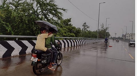திருச்சி ஜங்ஷன் மேம்பாலத்தில் குடைபிடித்தவாறு இருசக்கர வாகனத்தில் செல்லும் இளைஞர்கள்.