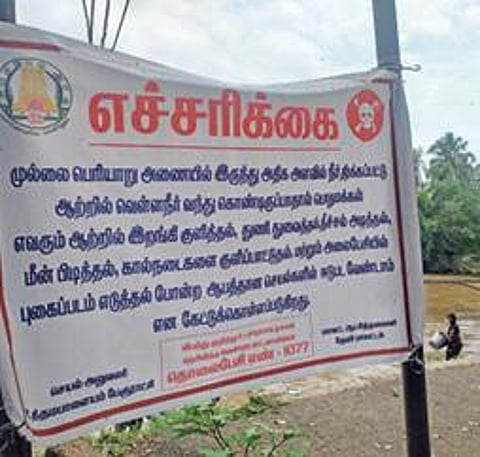 உத்தமபாளையம் முல்லை பெரியாற்றில் பேரூராட்சி சார்பில் வைக்கப்பட்டுள்ள எச்சரிக்கை பதாகை.