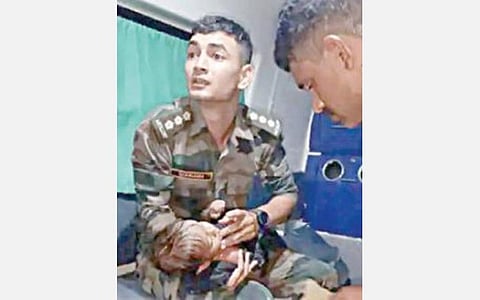 ஆம்புலன்ஸில் குழந்தையை கைகளில் ஏந்தியவாறு காணப் படும் ராணுவ வீரர்.