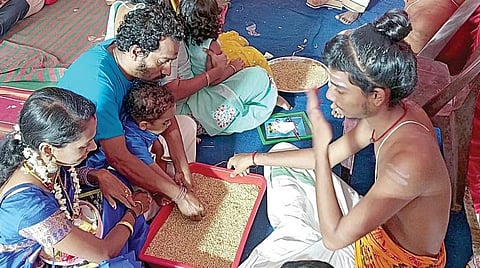தங்களுடைய குழந்தைக்கு நெல்மணிகளைப் பரப்பி எழுதவைத்து வித்யாரம்பம் செய்யும் பெற்றோர்.