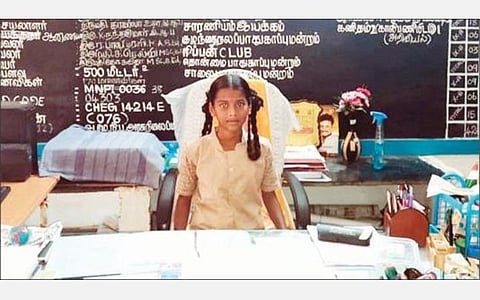 தலைமையாசிரியர் இருக்கையில் அமர்ந்துள்ள மாணவி பா.தனுஷ்.