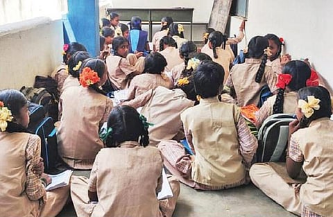 தேன்கனிக்கோட்டை அரசு பெண்கள் மேல்நிலைப் பள்ளியில் போதிய வகுப்பறை கட்டிட வசதியில்லாததால், நடைபாதையை வகுப்பறையாக்கி கல்வி பயிலும் மாணவிகள்.