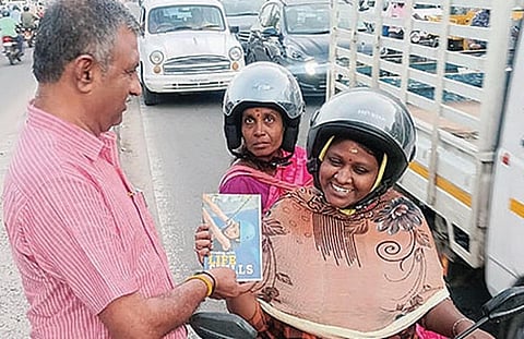 தலைக்கவசம் அணிந்து வந்த பெண்களுக்கு புத்தகப் பரிசு வழங்கிய சுரேஷ்குமார்.