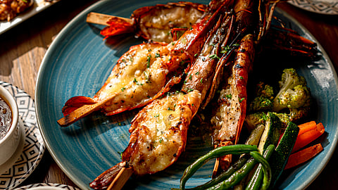 Close-up of Chimichurri jumbo prawns, served with grilled broccoli, zucchini, carrots, green beans and potato wedges on a blue ceramic plate.