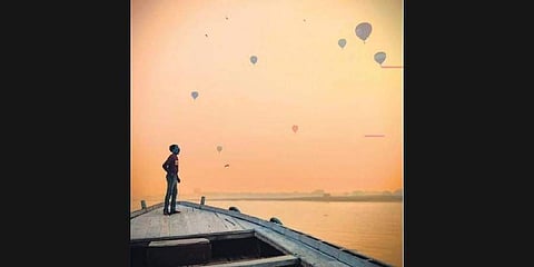 A boatman looks at the hot air balloons in the sky in Varanasi