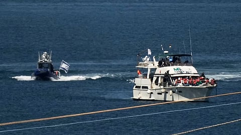 Activists in orange life jackets sit aboard a Gaza-bound Sumud flotilla boat as Israeli navy soldiers