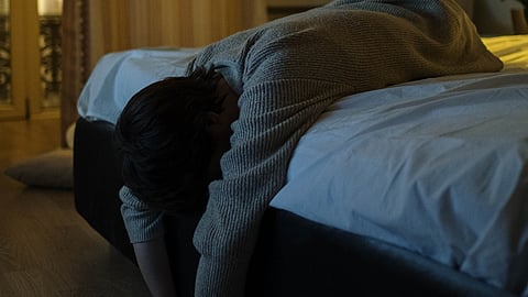 A person with gray long sleeves lying tiredly on a bed at night, feeling exhaustion and insomnia.