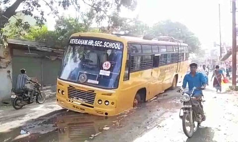  பள்ளிவாகனத்தின் சக்கரம் ரோட்டில் புதையுண்ட காட்சி.