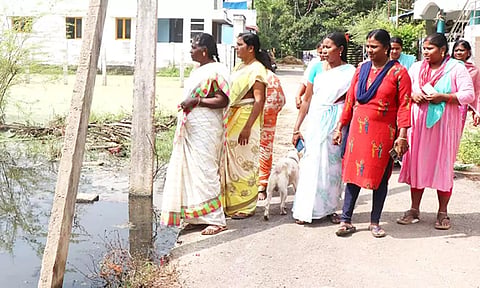 குடியிருப்புகளை சுற்றி தேங்கி நிற்கும் கழிவுநீரை வேதனையுடன் பார்க்கும் பெண்கள்.